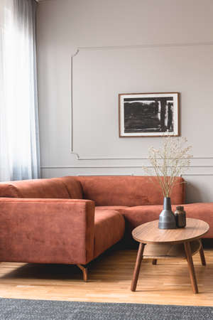 Dry flowers in stylish dark vase on wooden coffee table in front of ginger colored corner sofaの写真素材