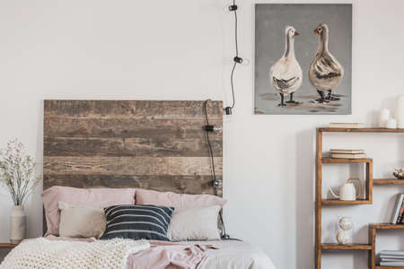 Cute ducks on grey oil painting in white rustic bedroom interior with fancy bookshelf and bed with wooden headboardの写真素材
