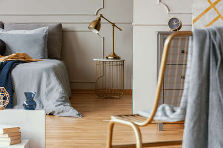 Trendy bedroom interior with grey commode and golden chairの写真素材