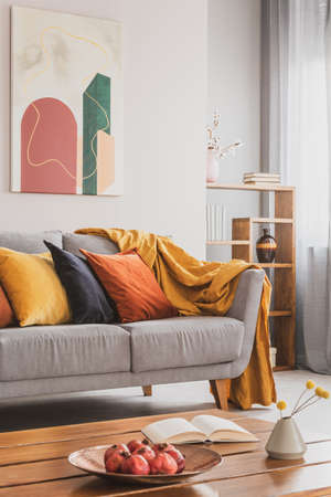 Yellow, orange, black and brown pillows on comfortable grey scandinavian sofa in bright living room interior with abstract paintings on the wallの写真素材