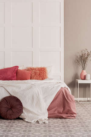 Amaranth pillow and dirty orange bedding on king size bed in fashionable bedroom interiorの写真素材