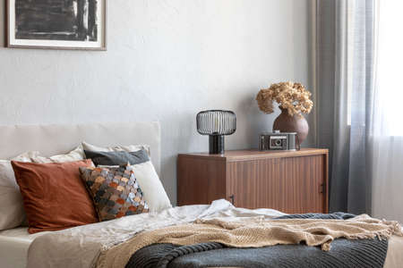 Vintage wooden cupboard next to king size bed with pillows and blanket in trendy bedroom interior