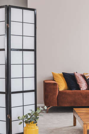 Yellow, black and pastel pink pillow on brown couch in grey living room interior, copy space on empty wallの写真素材