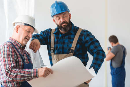 Two builders wearing helmets looking at the construction planの写真素材