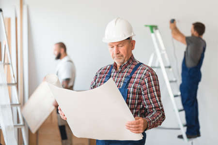 Older team leader of construction crew looking at the building sketchの写真素材