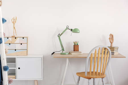 Pile of books, wooden hand and industrial mint colored lamp on stylish wooden desk in white kid's bedroomの写真素材