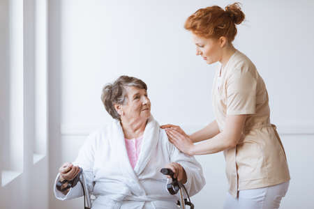 Young caring nurse helping older woman on a wheelchair