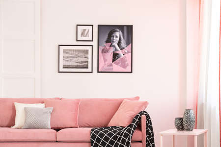 Gallery of posters on empty white wall of bright living room interior with pastel pink settee