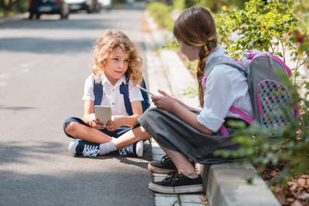 Boy and girl sitting on a pavement and playing on tabletsの写真素材