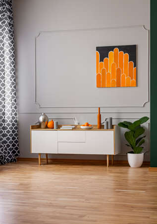 Abstract black and orange painting on empty grey wall of stylish room