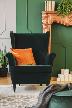 Comfortable emerald green armchair with orange pillow in fashionable living room interiorの写真素材