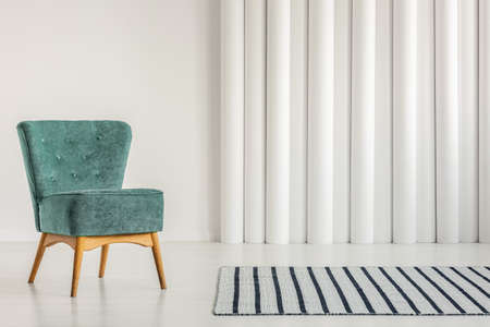 Stylish turquoise armchair in empty white interior with striped rugの写真素材