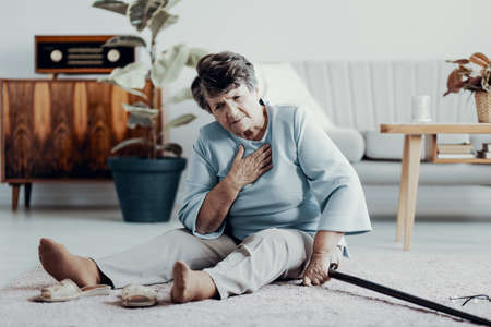 Weak senior woman with heart attack sitting alone at home with walking stickの写真素材