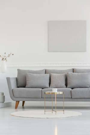 Small elegant coffee table in front of long scandinavian couch in bright daily room interiorの写真素材