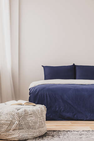 Empty bedroom interior with simple blue bed and book on pouf, copy space on the wall