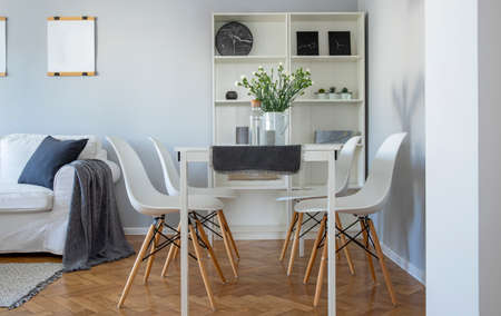 Flowers in vase on white dining table with four trendy chairs in stylish living room