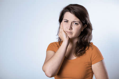Pretty young student woman with a aching tooth, copy space on empty backgroundの写真素材