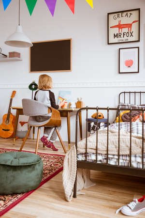 Cute little girl sitting at desk in her stylish vintage bedroom with workspaceの写真素材