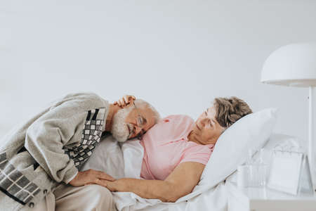 Older man supporting his terminally sick wife in a hospital bedの写真素材