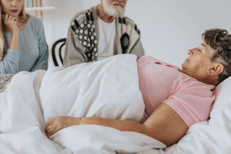Older woman dying in hospital bed surrounded by familyの写真素材