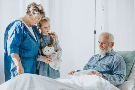 Young girl and grandmother supporting dying grandfather in hospitalの写真素材