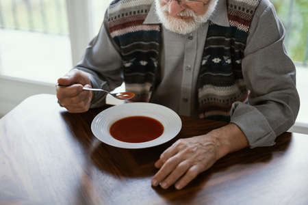 Close-up of older lonely man eating a soup in his homeの写真素材
