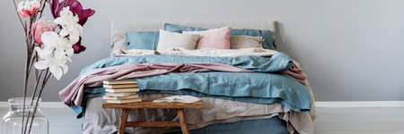Panoramic view of king size bed with pastel pink, blue and beige bedding next to wooden bench with...