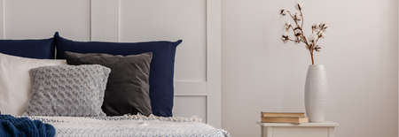 Cotton flower in white vase on trendy small table in white bedroom with blue bedding on bedの写真素材
