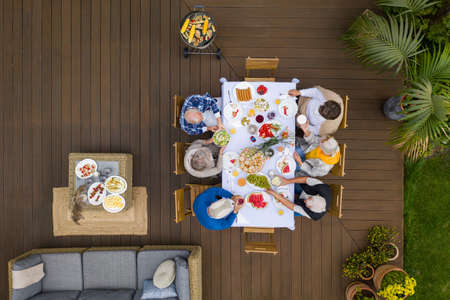 Group of senior friends sitting by the table and eating during garden partyの写真素材