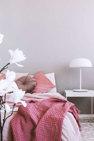 White industrial lamp on simple nightstand table next to cozy bed with pink beddingの写真素材