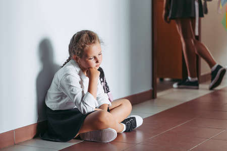 Sad young girl sitting alone on a school corridor during breakの写真素材