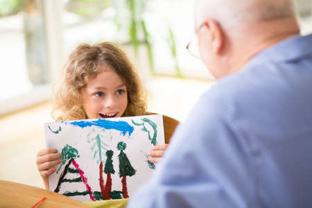 Cute little boy showing his painting to grandfatherの写真素材