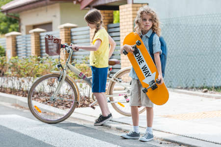 Girl on a bike and boy with a skateboard crossing the streetの写真素材