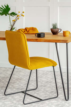 Stylish yellow chair at wooden dining table in trendy interior