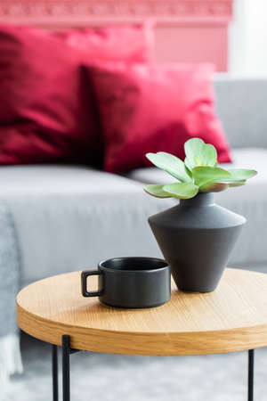 Green flowers in black vase next to black coffee cup on wooden coffee table in stylish interiorの写真素材