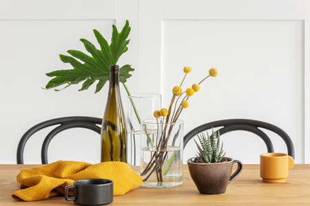 Yellow flowers in glass vase, a bottle of wine, washcloth and coffee cup on wooden dining table