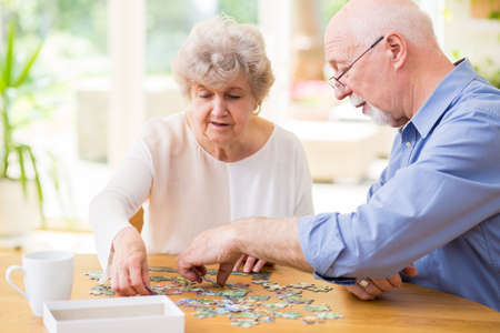 Cute grandma and grandpa put puzzle pieces together at homeの写真素材