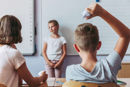 Rude young boy throwing a paper ball into the girl during classesの写真素材
