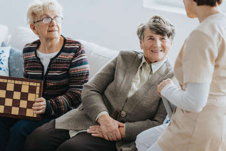 Older ladies sit on a couch and talk to a nurse at a local nursing homeの写真素材