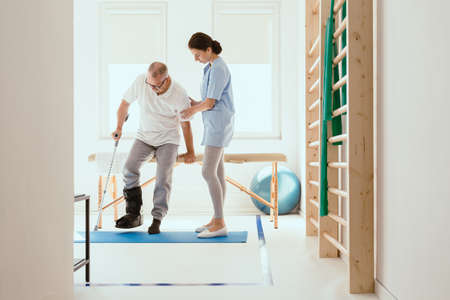 Young physiotherapist exercises in a bright medical office with his injured patient
