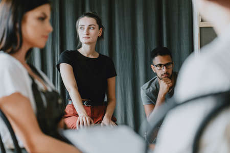 Young worried girl sitting on a group psychotherapy with friendsの写真素材