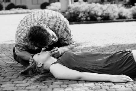 Black and white photo of a man leaning over a woman in the street and checking her life functions