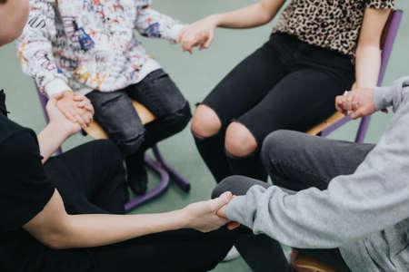 Close-up of four people sitting together in a circle, holding handsの写真素材