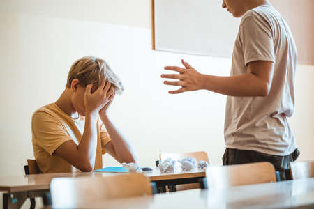 Mean boys bullying a classmate sitting at school deskの写真素材