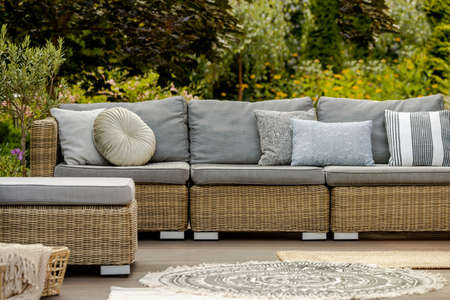 Grey pillows on trendy wicker L shape sofa in the green gardenの写真素材