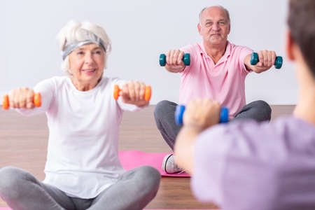 Couple of active seniors during exercises on gym with young instructorの写真素材