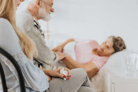 Loving family taking care of older sick woman in hospital bed
