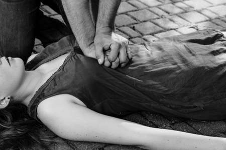 Black and white photo of man giving first aid to a woman during an street accidentの写真素材