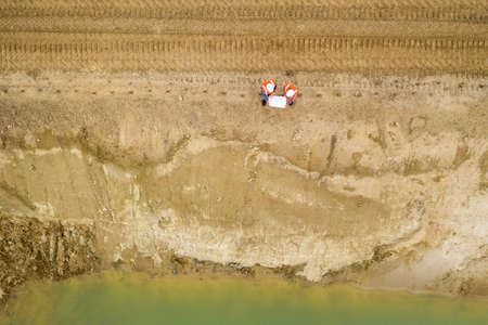 Top view of two road construction workers in orange vests and protective helmets in the middle on...