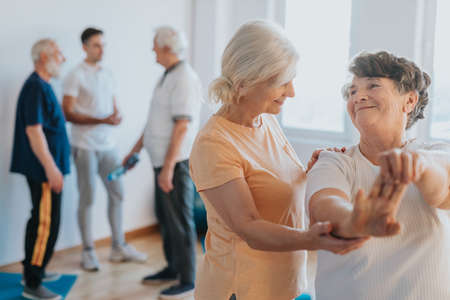 Senior instructor showing older woman how to stretch the musclesの写真素材